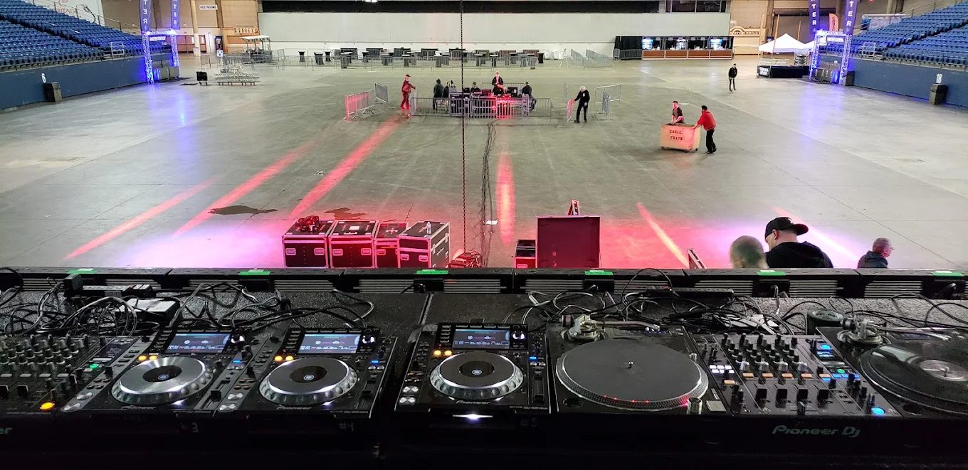 DJ booth set up on a large arena floor ahead of a corporate event