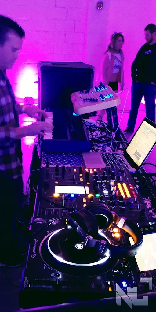 A DJ producing a set on a keyboard and controller, framed by purple stage lighting