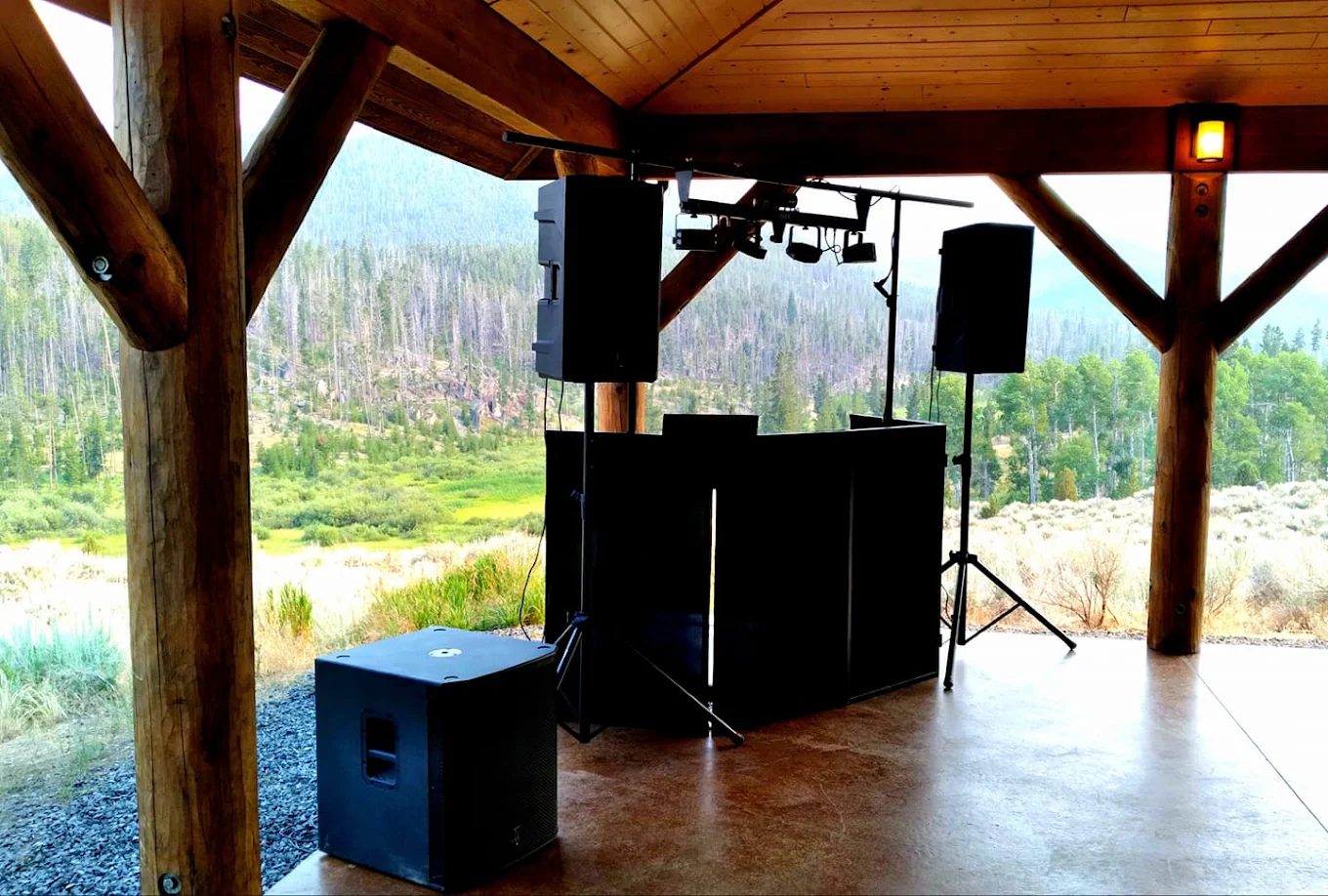 DJ equipment set up under a covered pavilion overlooking a mountain valley